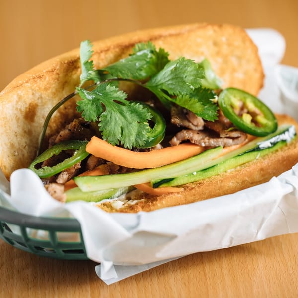 A Vietnamese banh mi sandwich with meat, cilantro, jalapeños, carrots, and cucumbers in a basket.