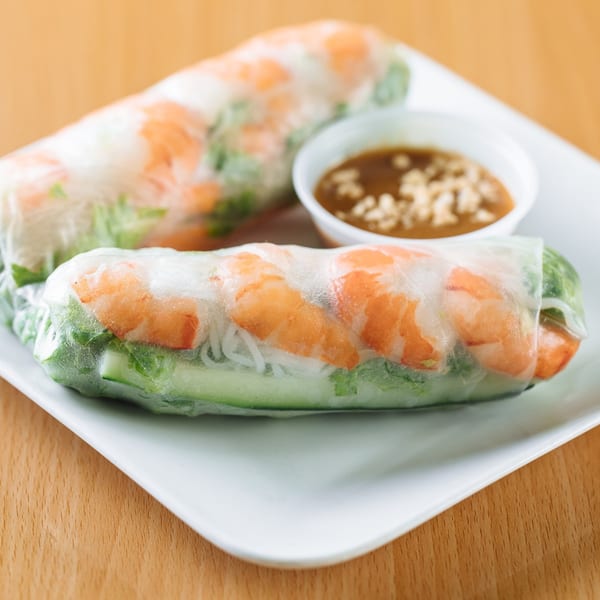 Two fresh Vietnamese spring rolls filled with shrimp, noodles, and greens, with peanut sauce.