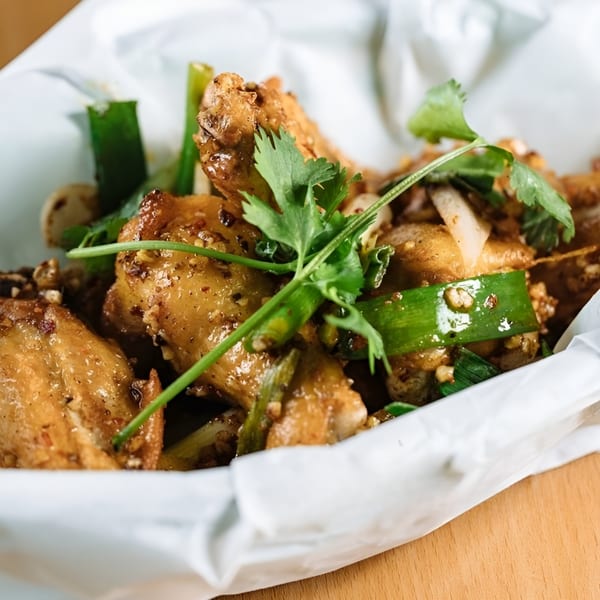 Close-up of Vietnamese chicken wings with green onions and cilantro in a white paper-lined basket.