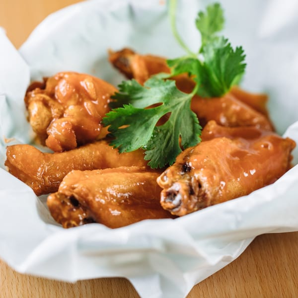 Sweet and sour chicken wings garnished with cilantro, served in a white paper-lined basket.
